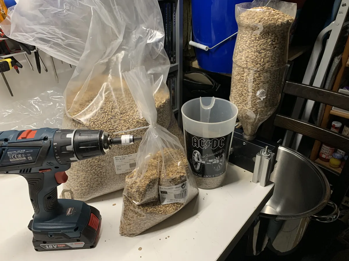 Schrotmühle mit Akkuschrauber auf dem Tisch, daneben Säcke mit Malz