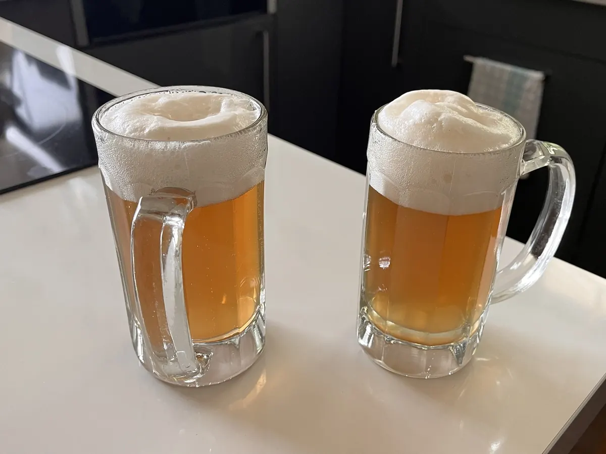 Zwei Humpen helles Bier mit dicker Schaumkrone auf einem Tisch